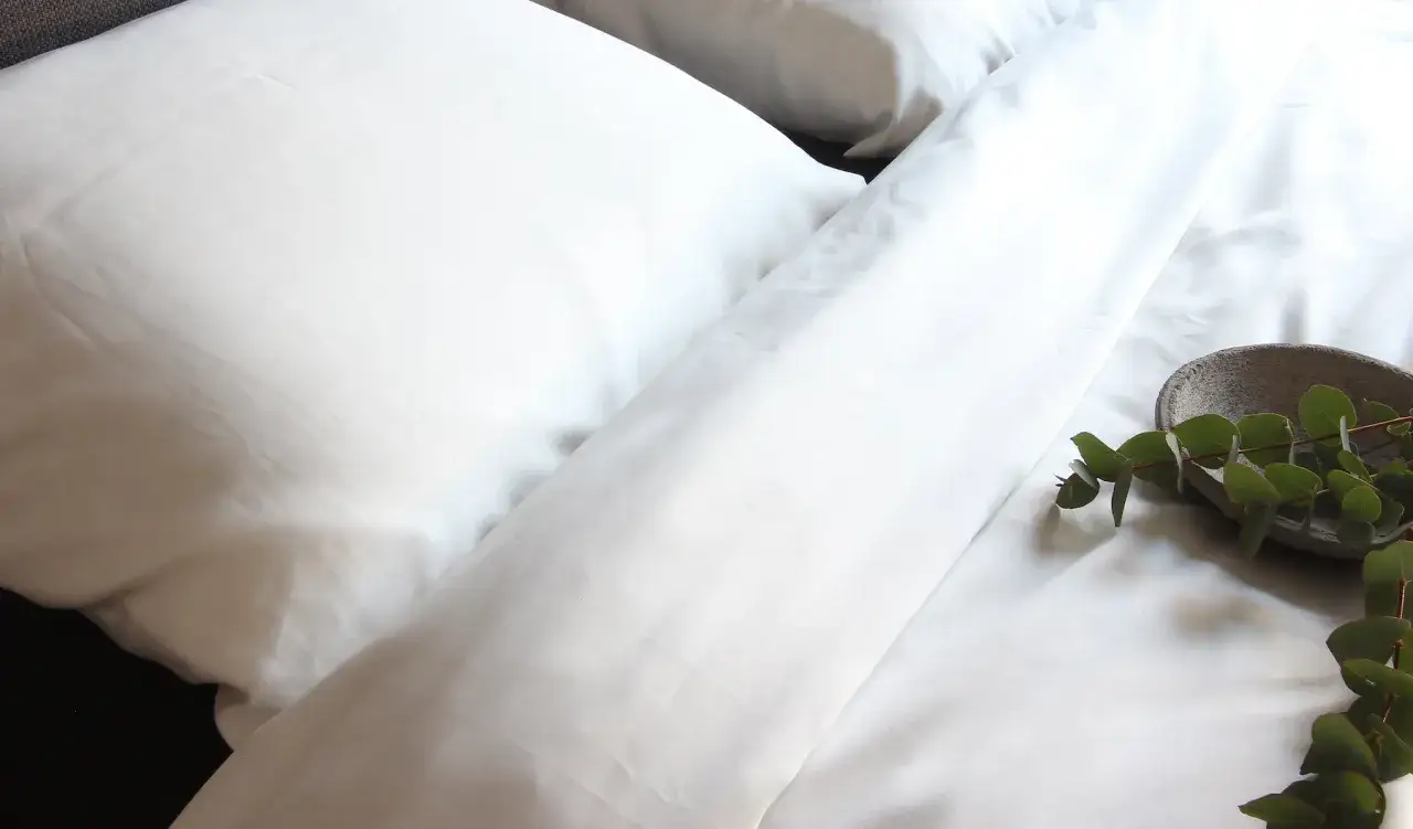 Ein frisch bezogenes Bett mit wei&szlig;en Laken und Kissen. Ein kleiner Steinbeh&auml;lter mit Eukalyptuszweigen liegt auf dem Bett. Die Frage, wie viel schwitzt man in der Nacht, besch&auml;ftigt viele.