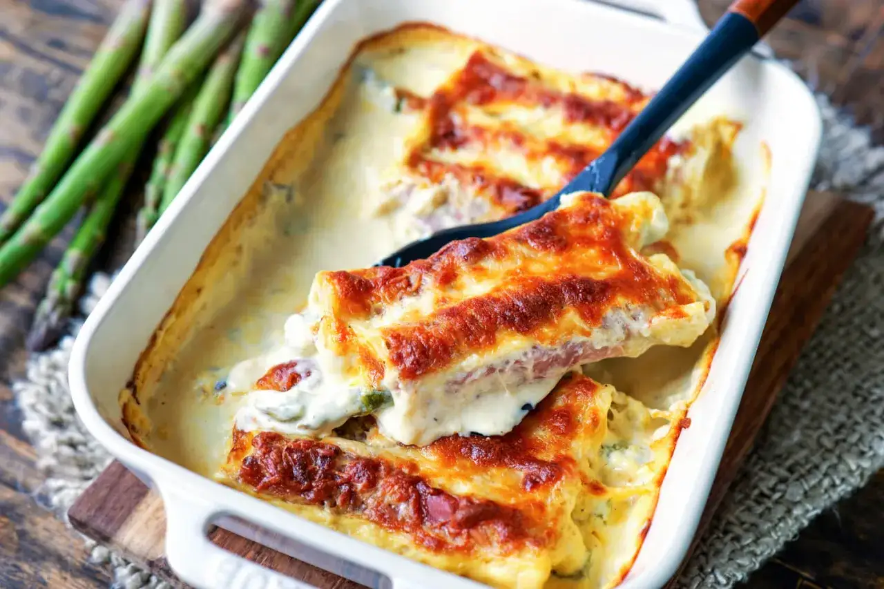 &Uuml;berbackene Spargel-Cannelloni in cremiger Sauce, goldbraun gebacken. Daneben ein Bund frischer gr&uuml;ner Spargel.