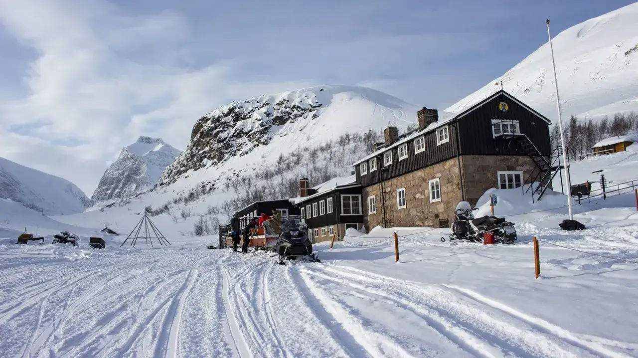 Vinterlandskap vid STF Kebnekaise fjällstation med snöskotrar och snöklädda berg.