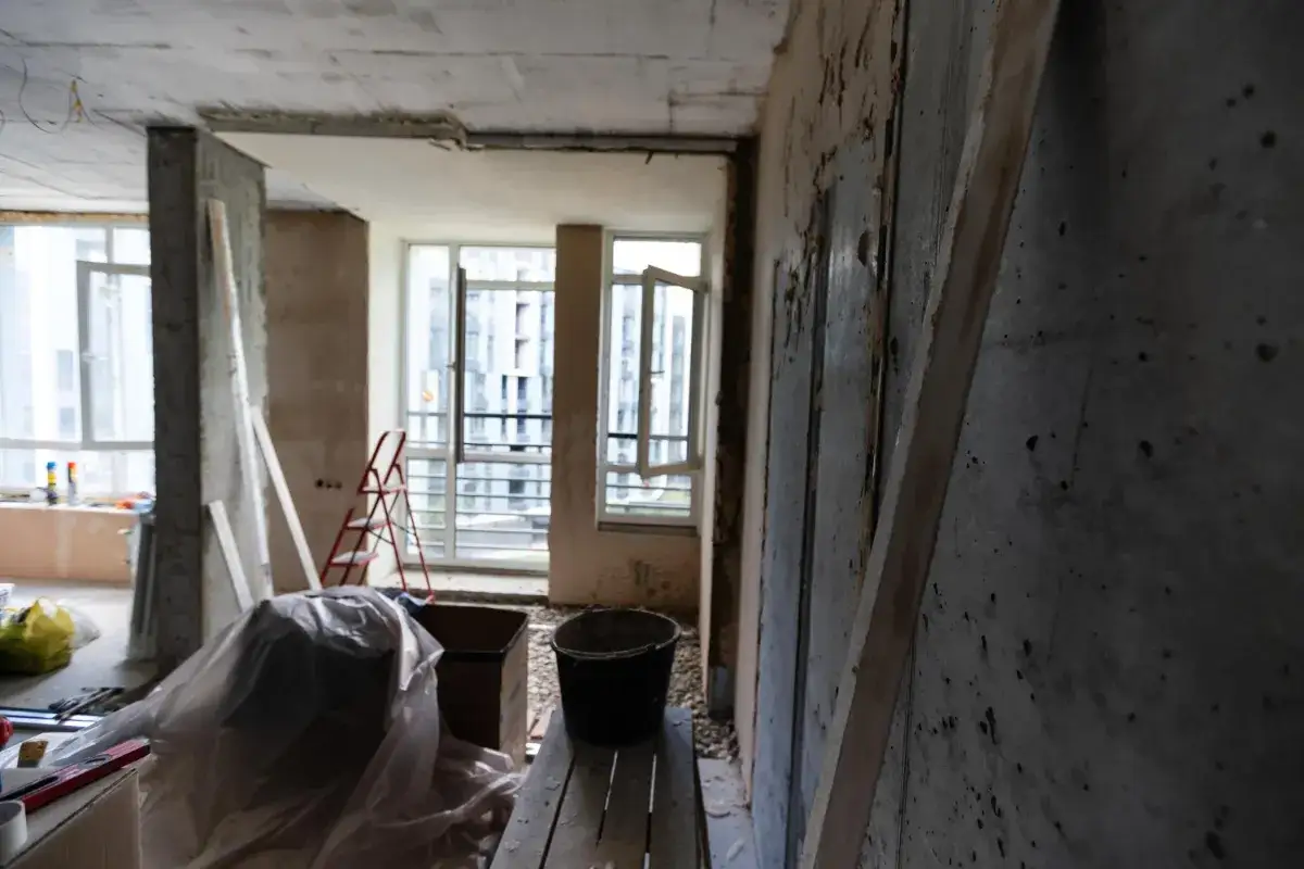 Remont mieszkania pod flip nieruchomości. Widoczne okna, drabina, wiadro i materiały budowlane.