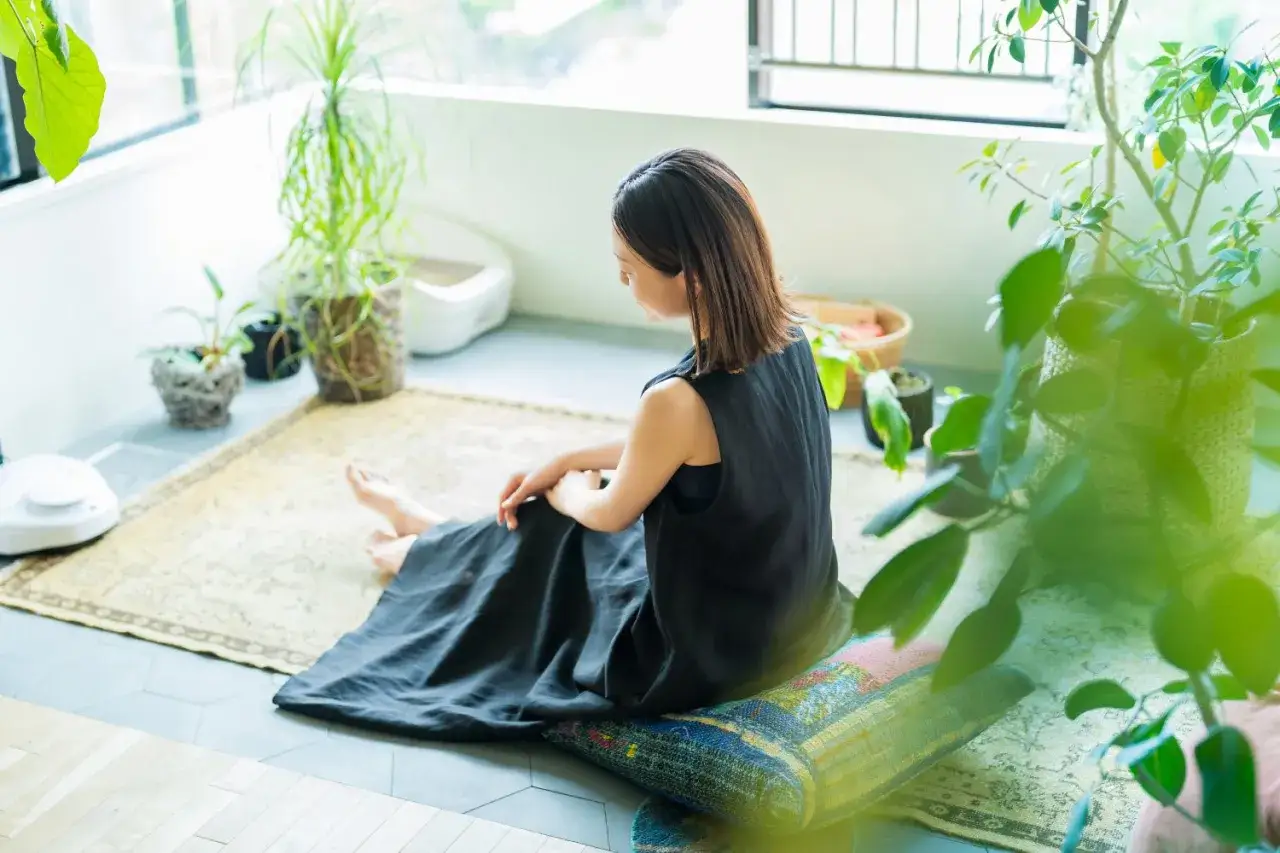 A woman in a black dress sits on a rug surrounded by plants, enjoying a moment of living a quiet life.