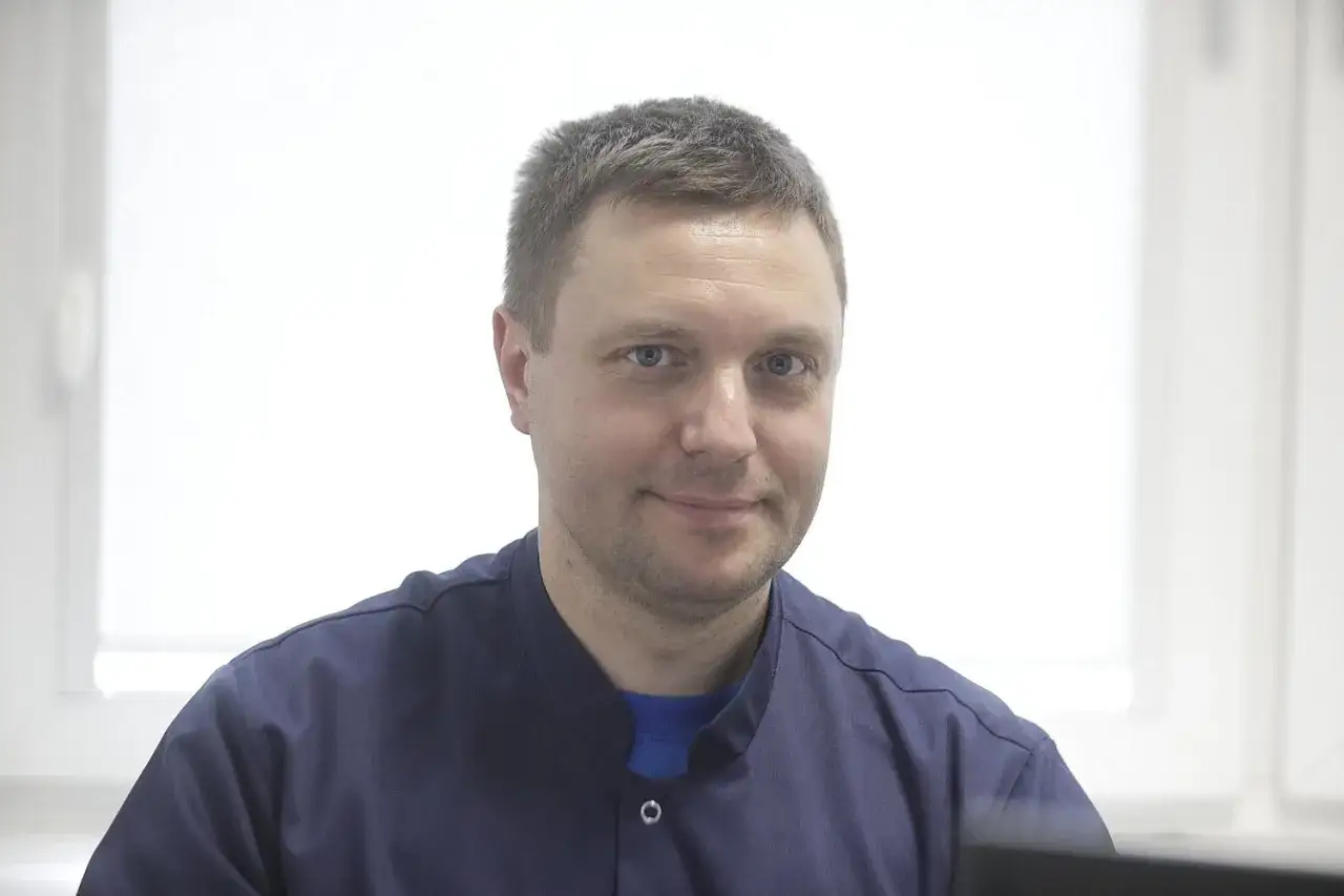 Portret mężczyzny w granatowym uniformie medycznym, patrzącego w obiektyw.