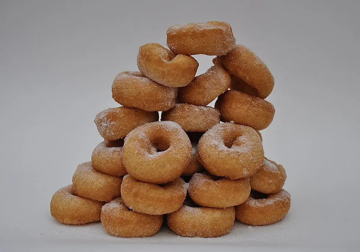 Montón de rosquillas de palo cubiertas de azúcar, apiladas en forma de pirámide sobre un fondo blanco.