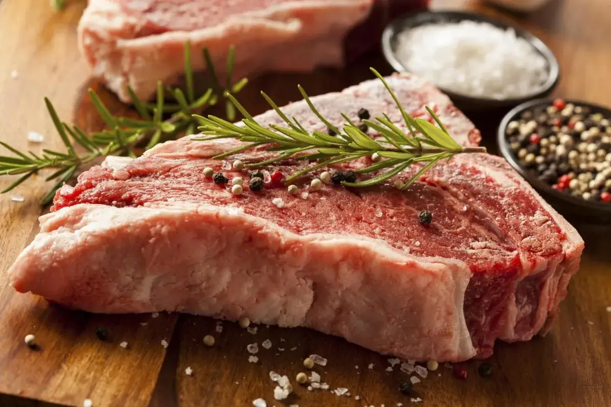 Bistecca alla fiorentina, un cibo succulento pronto per essere cucinato, con rosmarino, sale grosso e pepe.