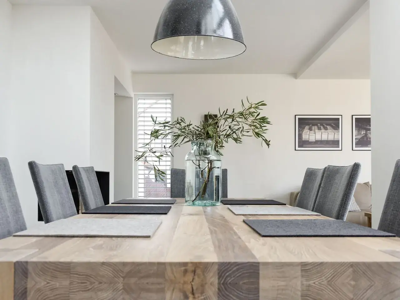 Holztisch mit grauen Filz-Platzsets und einer Vase mit Zweigen. Graue St&uuml;hle stehen bereit f&uuml;r ein gemeinsames Essen.