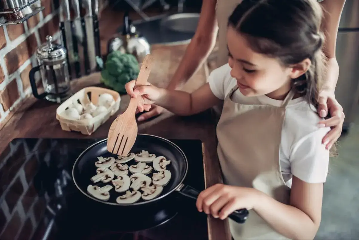 Mała kucharka smaży pieczarki na patelni. Czy dzieci mogą jeść pieczarki? Tak, to zdrowy dodatek do posiłków!