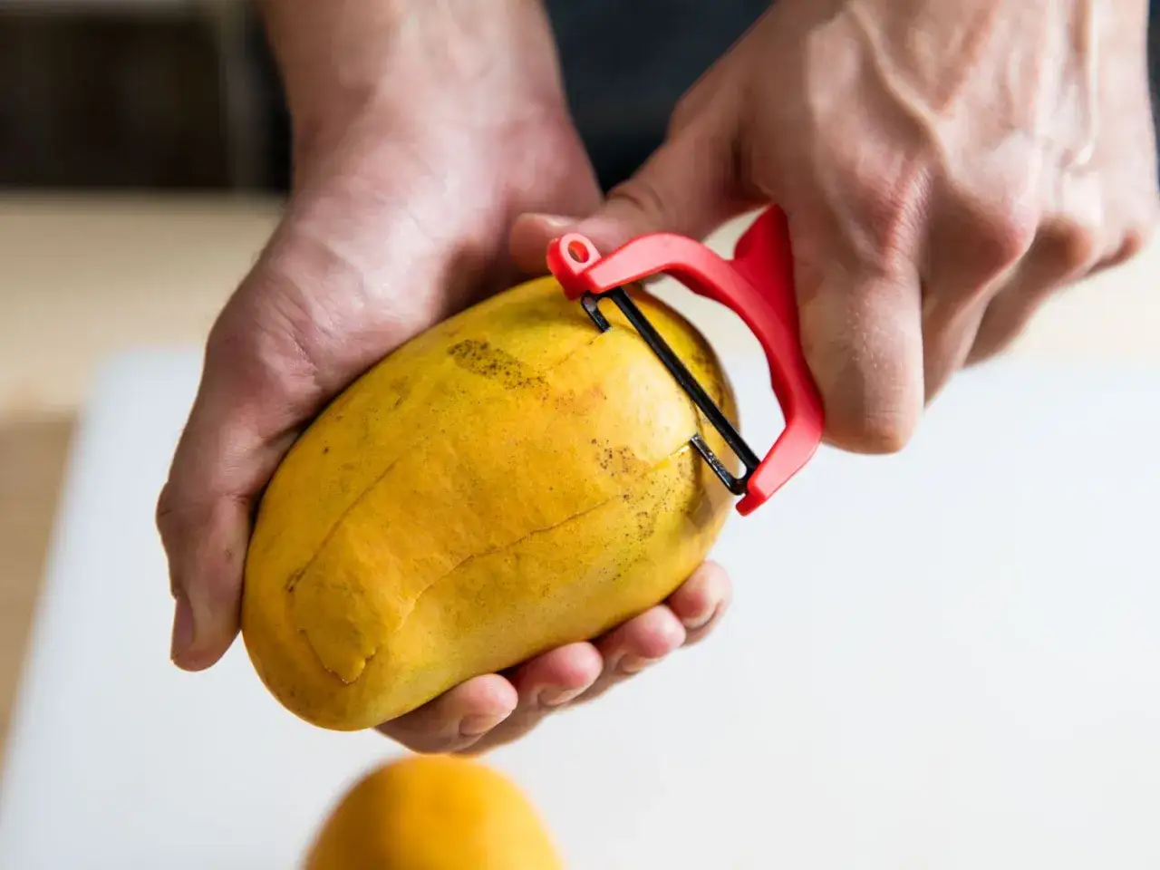 Ręce obierają dojrzałe mango. Warto znać mango przeciwwskazania, np. przy alergiach.