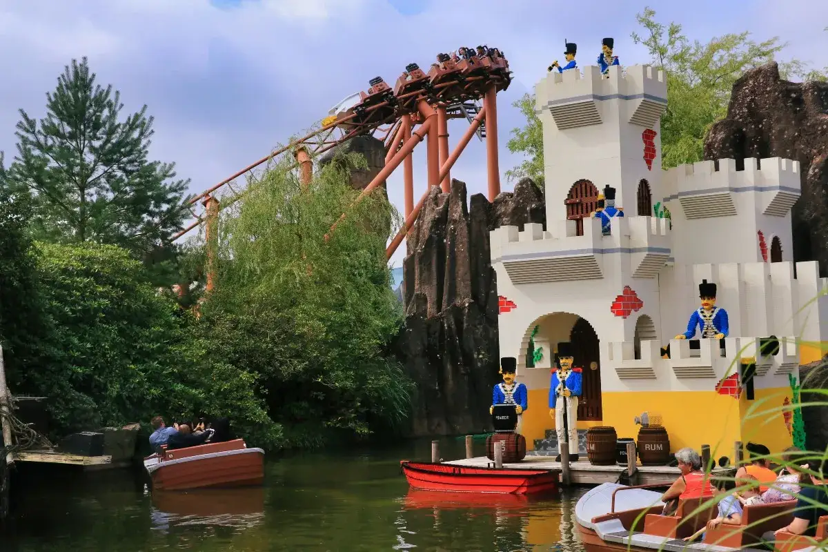 Zamek z klocków Lego w Legolandzie w Danii, z kolejką górską w tle i łodziami na wodzie.