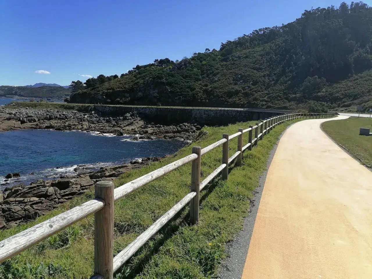 Un camino costero en A Guarda, Baiona, con valla de madera y mar azul.