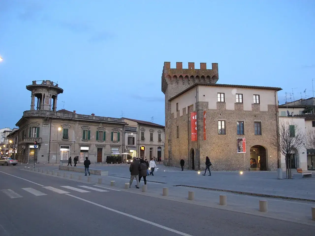 Piazza del centro storico di Montevarchi con edifici storici, tra cui una torre medievale e un palazzo con un loggiato.