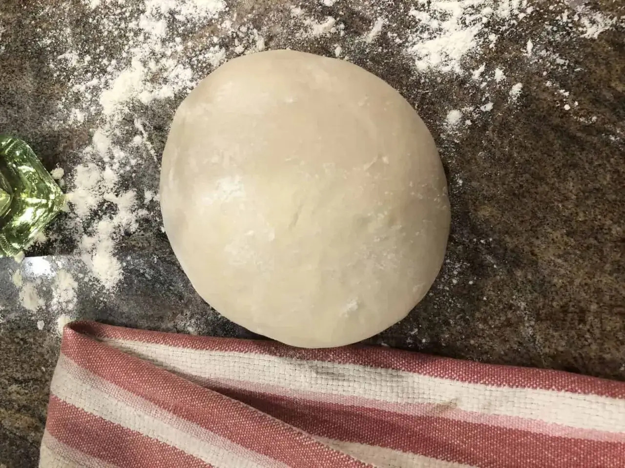 En perfekt rund deg för italiensk pizzadeg recept, redo att bakas. Lite mjöl på bänken och en randig kökshandduk.