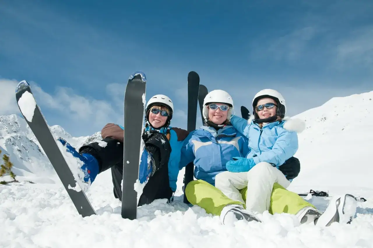 Glad familj p&aring; skidresa i Alperna. De sitter i sn&ouml;n med skidorna redo f&ouml;r mer &aring;kning.
