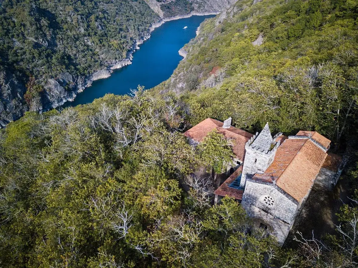 El monasterio Santa Cristina, rodeado de frondosa vegetación, se alza majestuoso junto a un río azul intenso.