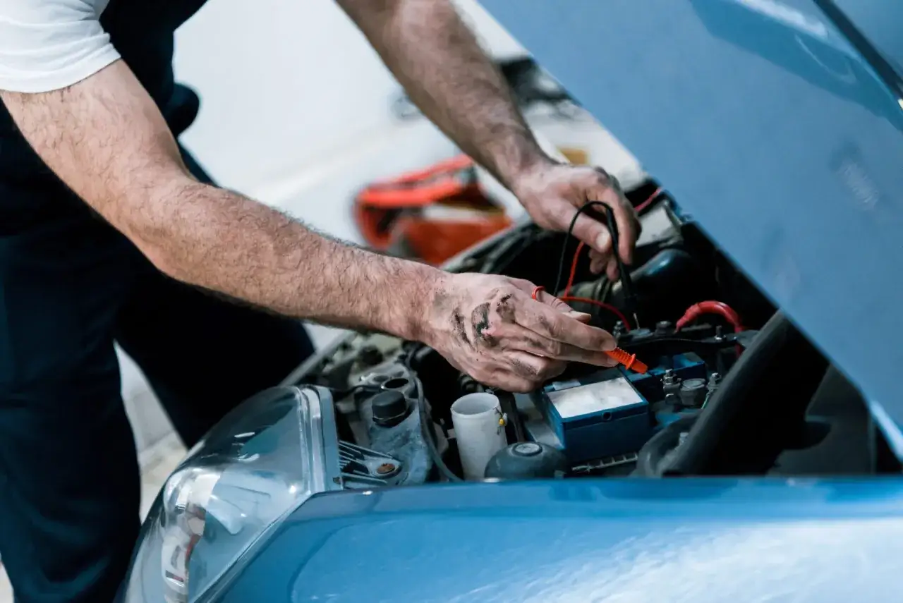 Mechanic checks car battery with multimeter, possibly diagnosing a p0302 code.