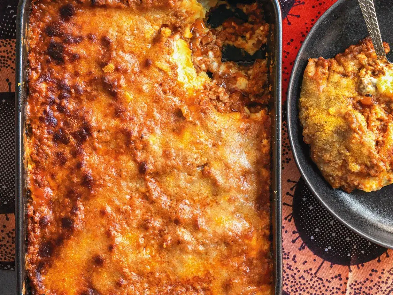Lasagne al ragù appena sfornate, dorate e filanti, con una porzione servita su un piatto nero.