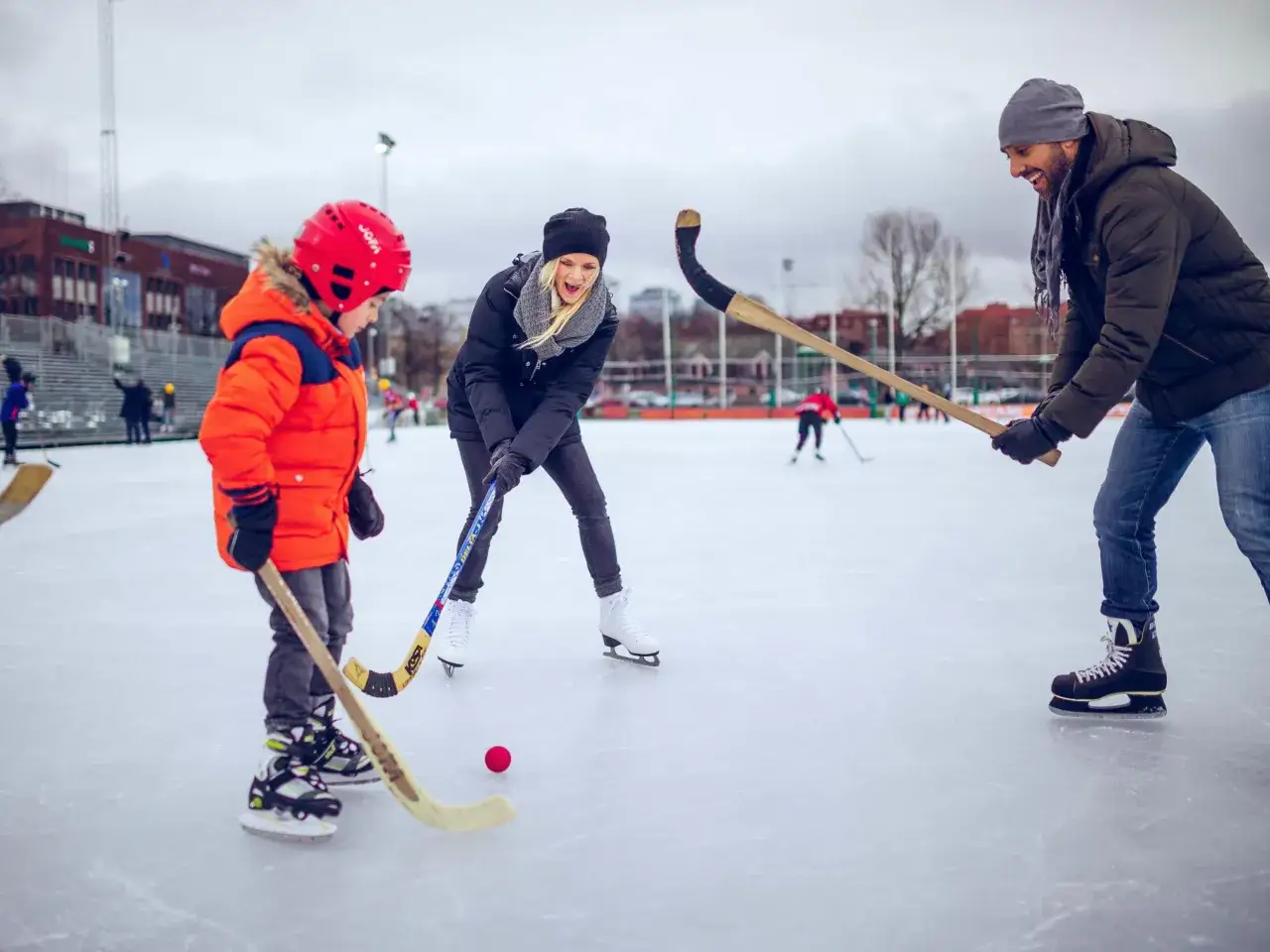 Familj spelar bandy på isen i Göteborg. En pappa, mamma och barn njuter av en aktiv dag med skridskoåkning och puckspel.