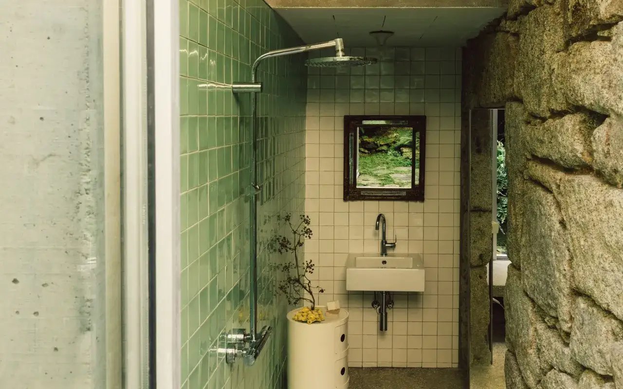 Ba&ntilde;os modernos peque&ntilde;os con azulejos verdes y blancos, lavabo minimalista y ducha. Un espejo refleja un jard&iacute;n exuberante.