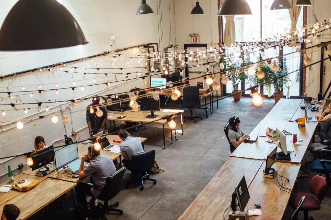 Bureau moderne avec plusieurs personnes travaillant sur leurs ordinateurs. L'espace ouvert favorise la collaboration et la cr&eacute;ativit&eacute;, avec des guirlandes lumineuses ajoutant une touche chaleureuse.