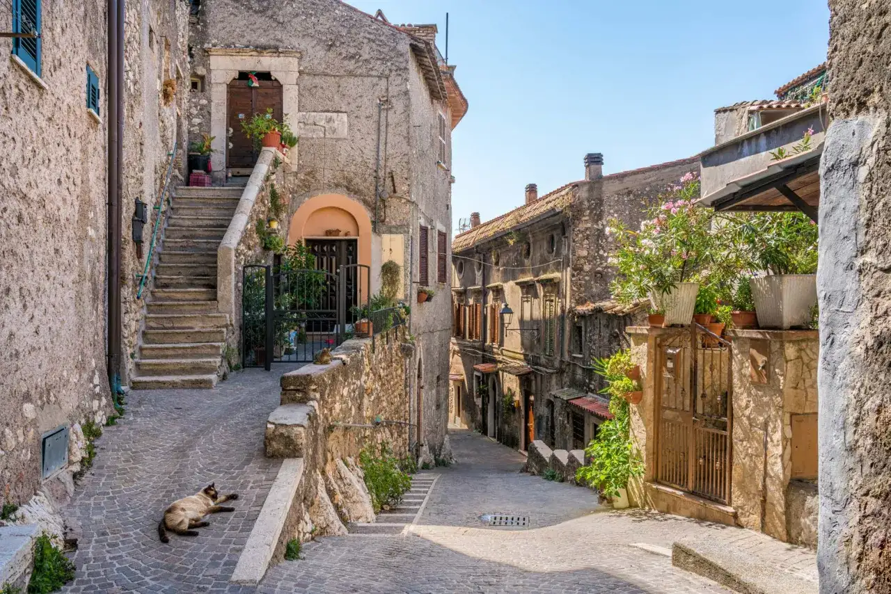 Un gatto si gode il sole in un vicolo acciottolato di uno dei tanti borghi da visitare, con case in pietra e scale che salgono.