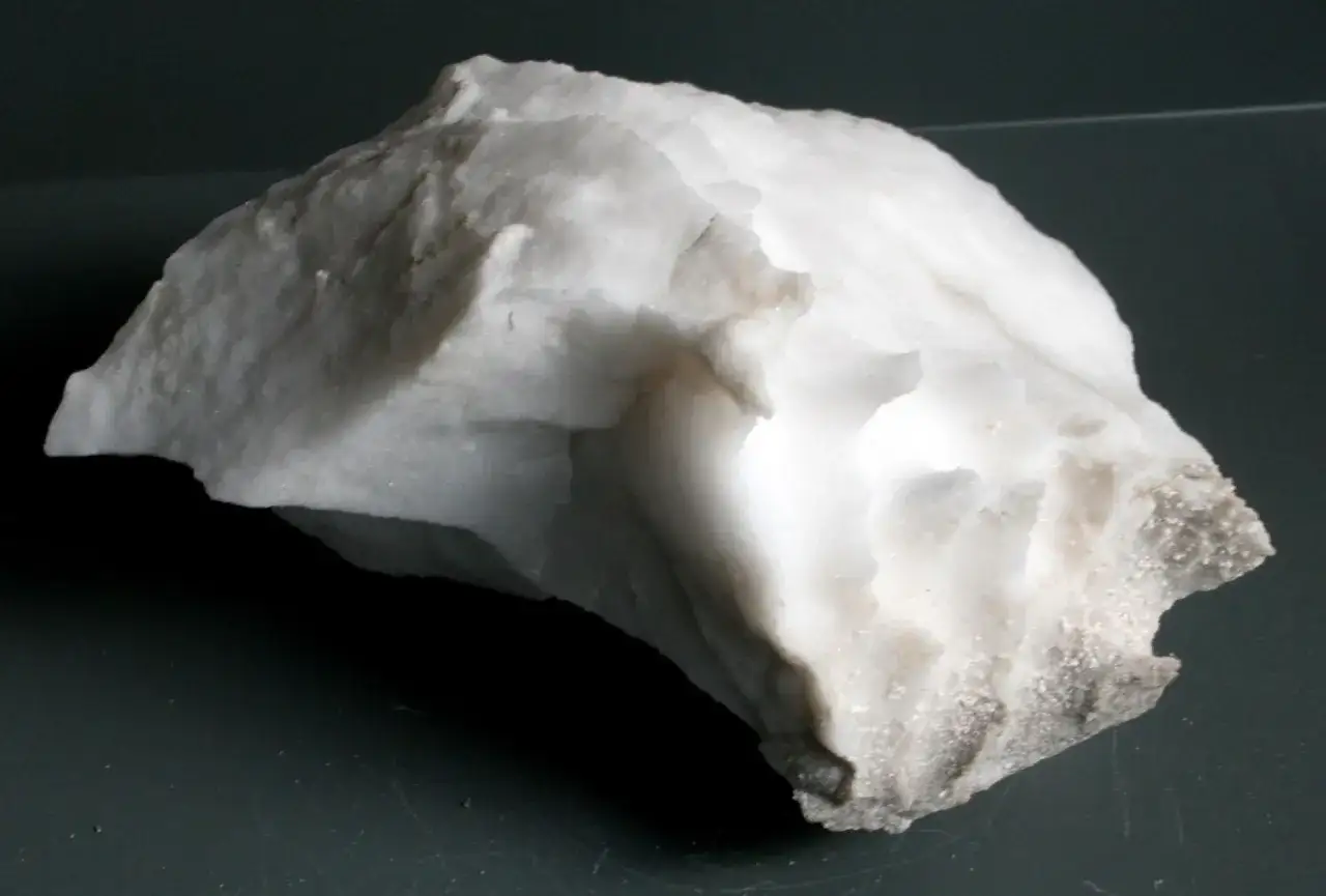Biały, matowy kamień przypominający alabaster, o nieregularnym kształcie i chropowatej powierzchni.