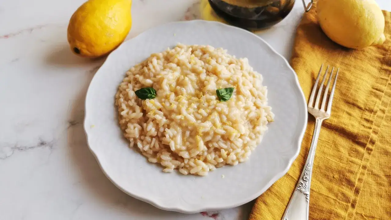 Un cremoso risotto al limone, guarnito con basilico e scorza di limone, pronto per essere gustato.