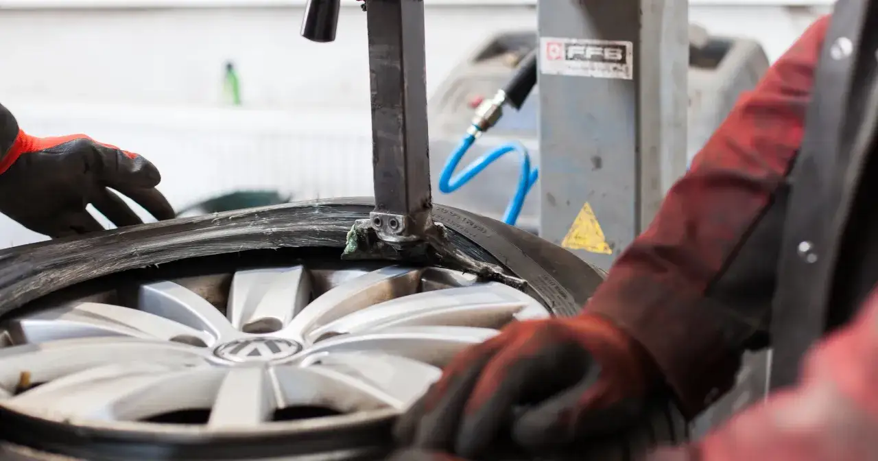 Mechanik w rękawiczkach dokonuje wymiany koła w samochodzie, używając specjalistycznego sprzętu do opon.