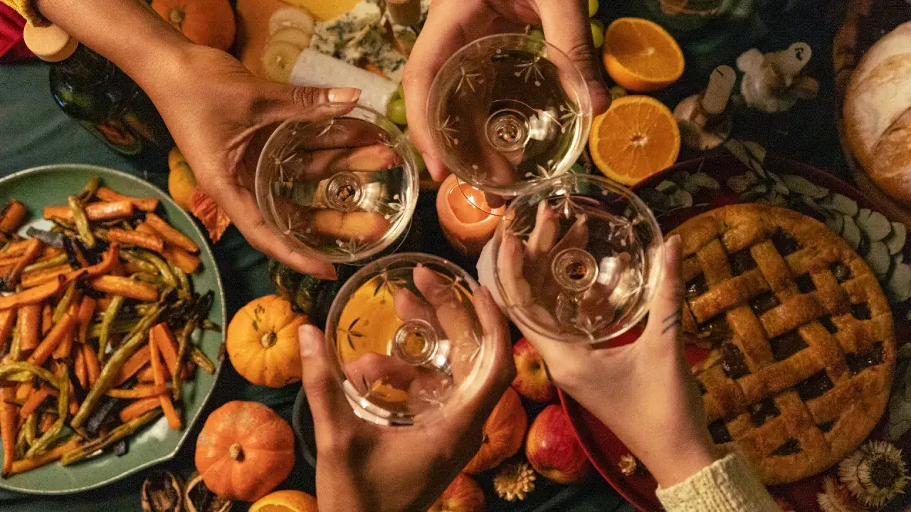 Hälsning med glas fyllda med vitt vin, perfekt till pumpasoppa. Bordet dignar av höstens godsaker: rostade grönsaker, äppelpaj och små pumpor.