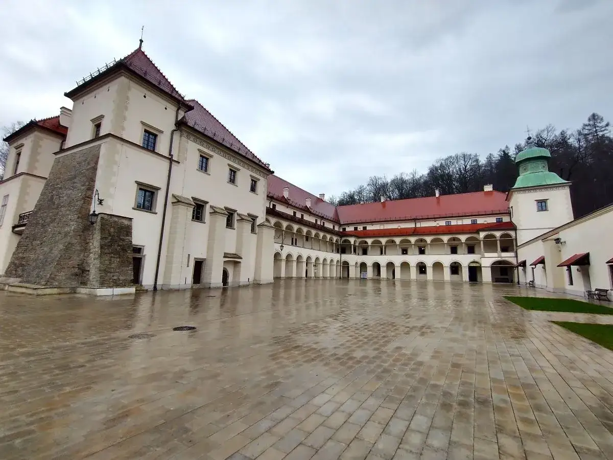 Zamek Sucha Beskidzka z arkadowym dziedzińcem i wieżą z zieloną kopułą, po deszczu.