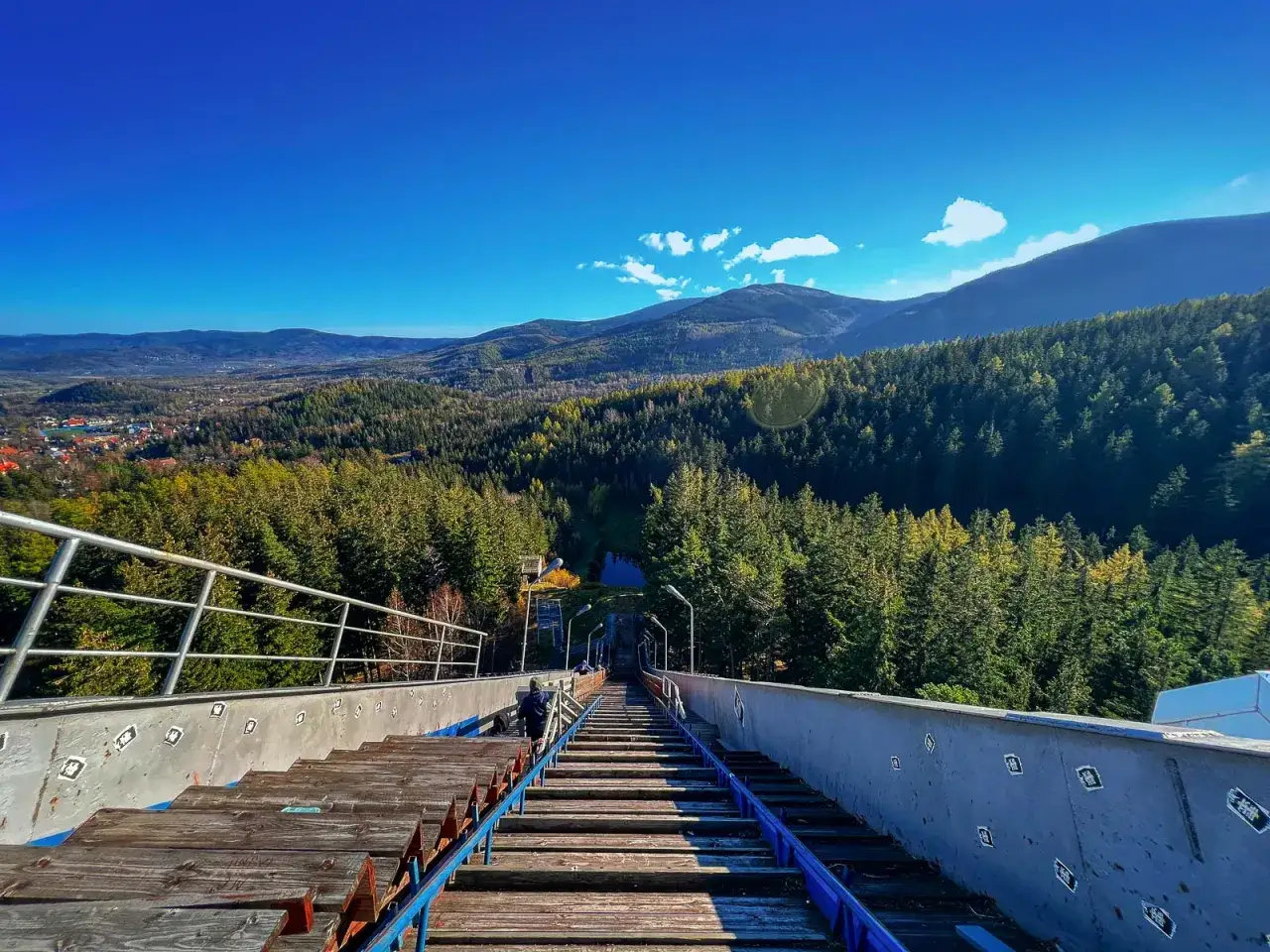 Widok z góry skoczni narciarskiej w Karpaczu. W dole las i miasto. Spacer w chmurach Karpacz cennik - warto sprawdzić przed wizytą.
