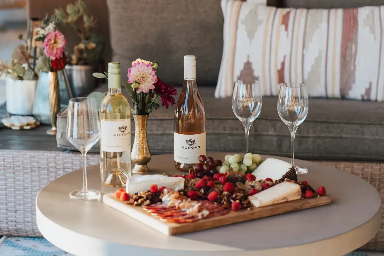 Ein Tisch mit Sauvignon Blanc, K&auml;se, Fr&uuml;chten und Aufschnitt. Blumen in einer Vase schm&uuml;cken die Szene.