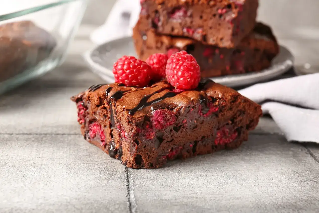 Pyszne brownie z malinami, polane czekoladą i ozdobione świeżymi malinami. Idealne na deser!
