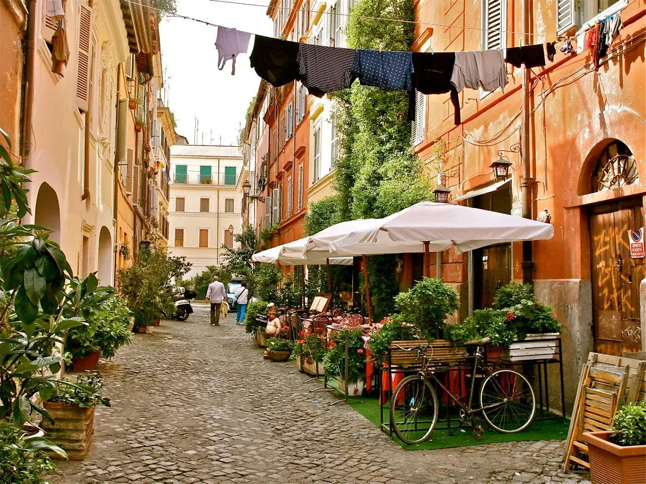 Un vicolo pittoresco a Trastevere, con panni stesi, un ristorante all'aperto e una bicicletta. Perfetto per scoprire cosa fare a Trastevere.