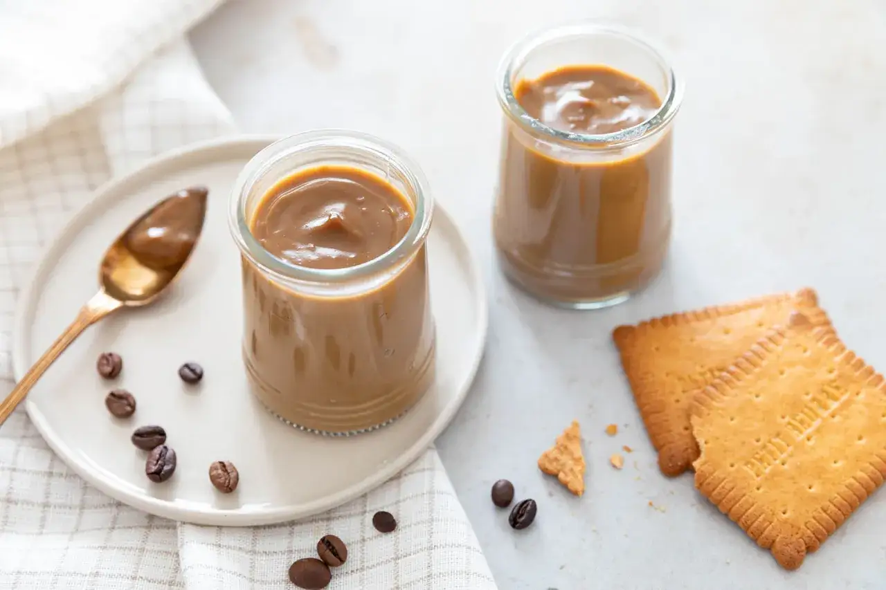 Deux pots de crème au café façon Danette, avec une cuillère dorée, des grains de café et des biscuits.