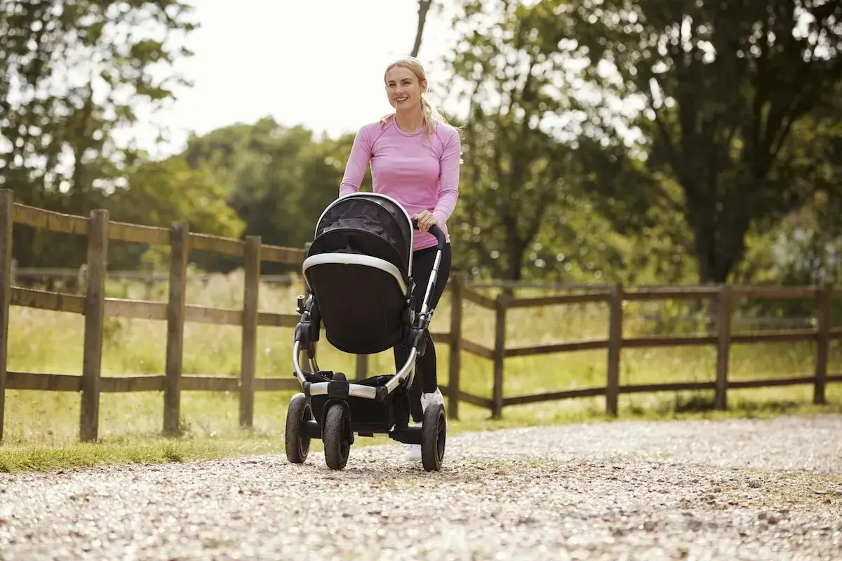Szczęśliwa mama spaceruje z wózkiem, szukając inspiracji, jak schudnąć po ciąży. Aktywność fizyczna na świeżym powietrzu to świetny początek!