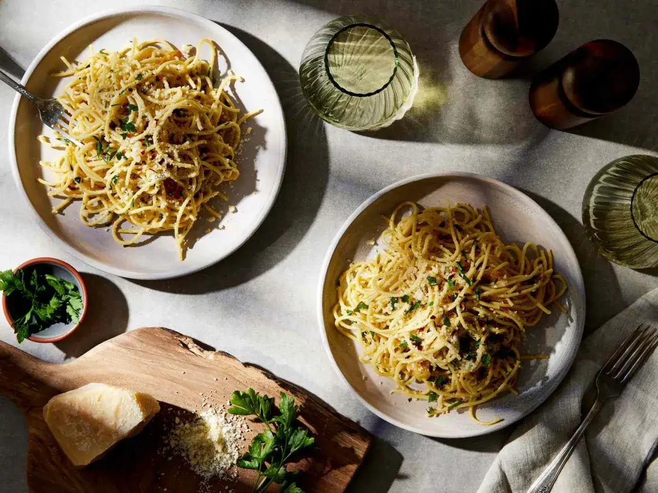 Dwa talerze pysznego spaghetti aglio, posypane parmezanem i natką pietruszki, gotowe do podania.