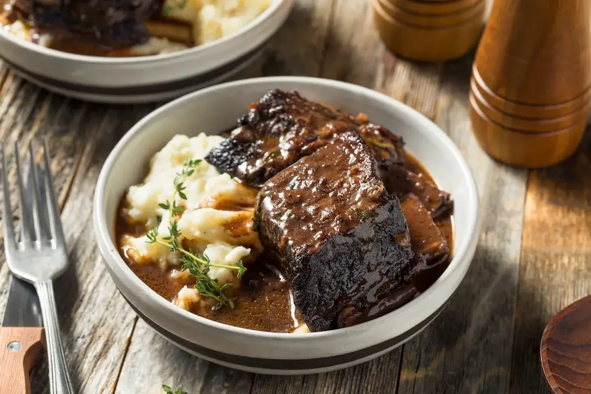 Un invitante brasato di manzo succulento servito con pur&egrave; di patate cremoso e guarnito con timo fresco.