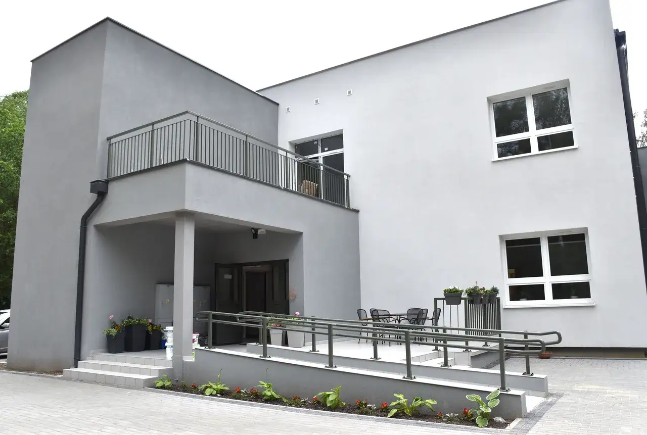 Nowoczesny budynek, przypominający dom dziecka po angielsku (children's home), z szarym tynkiem, balkonem i rampą.