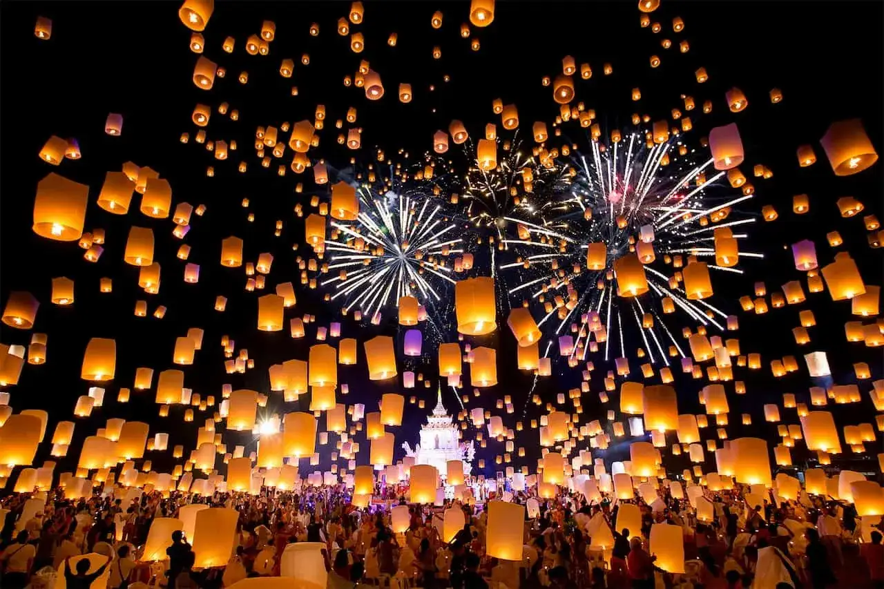 Tausende Himmelslaternen steigen bei einem Lichterfest in Thailand in den Nachthimmel, begleitet von einem Feuerwerk.