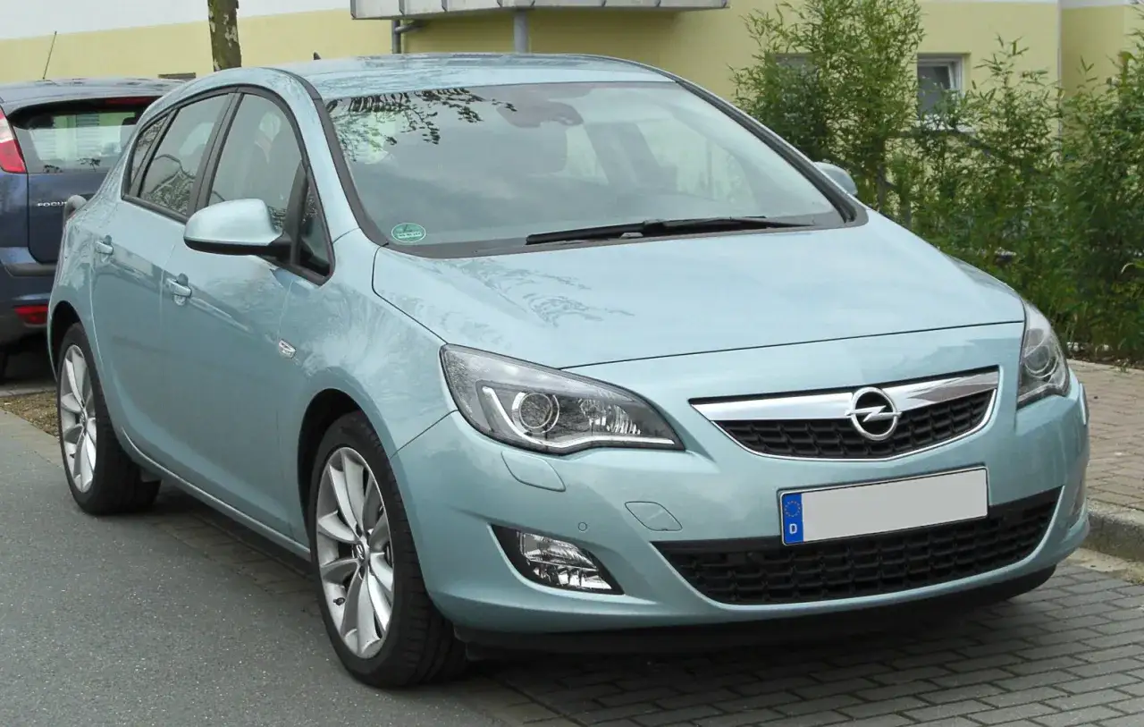 Jasnoniebieski Opel Astra J 1.6 benzyna zaparkowany na chodniku.