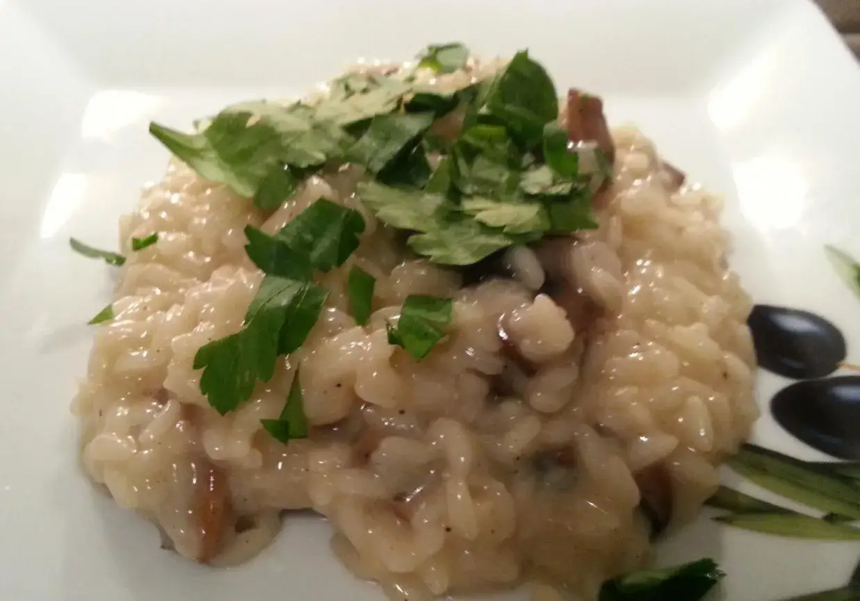 Kremowe risotto z boczniakami, udekorowane świeżą natką pietruszki, prezentuje się apetycznie na białym talerzu.