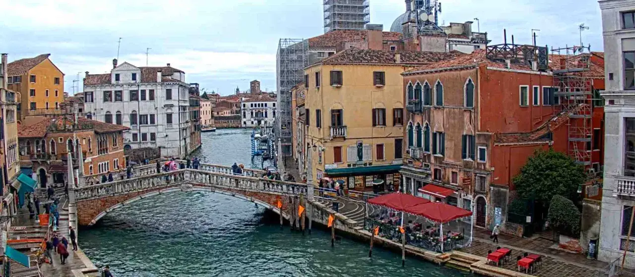 Il ponte delle Guglie attraversa un canale veneziano, circondato da edifici storici e persone che passeggiano.