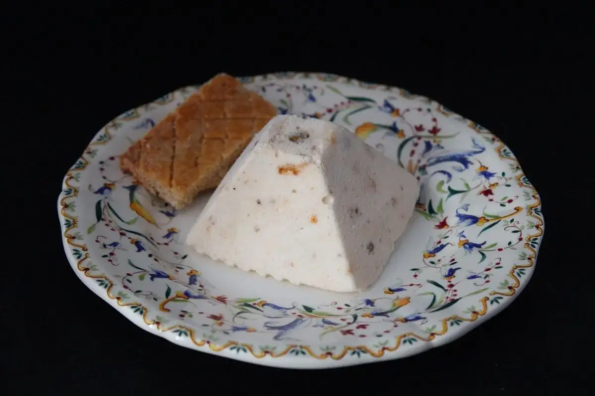 Un d&eacute;licieux nougat glac&eacute; en forme de pyramide, parsem&eacute; de fruits secs, repose sur une assiette orn&eacute;e de fleurs bleues et rouges.
