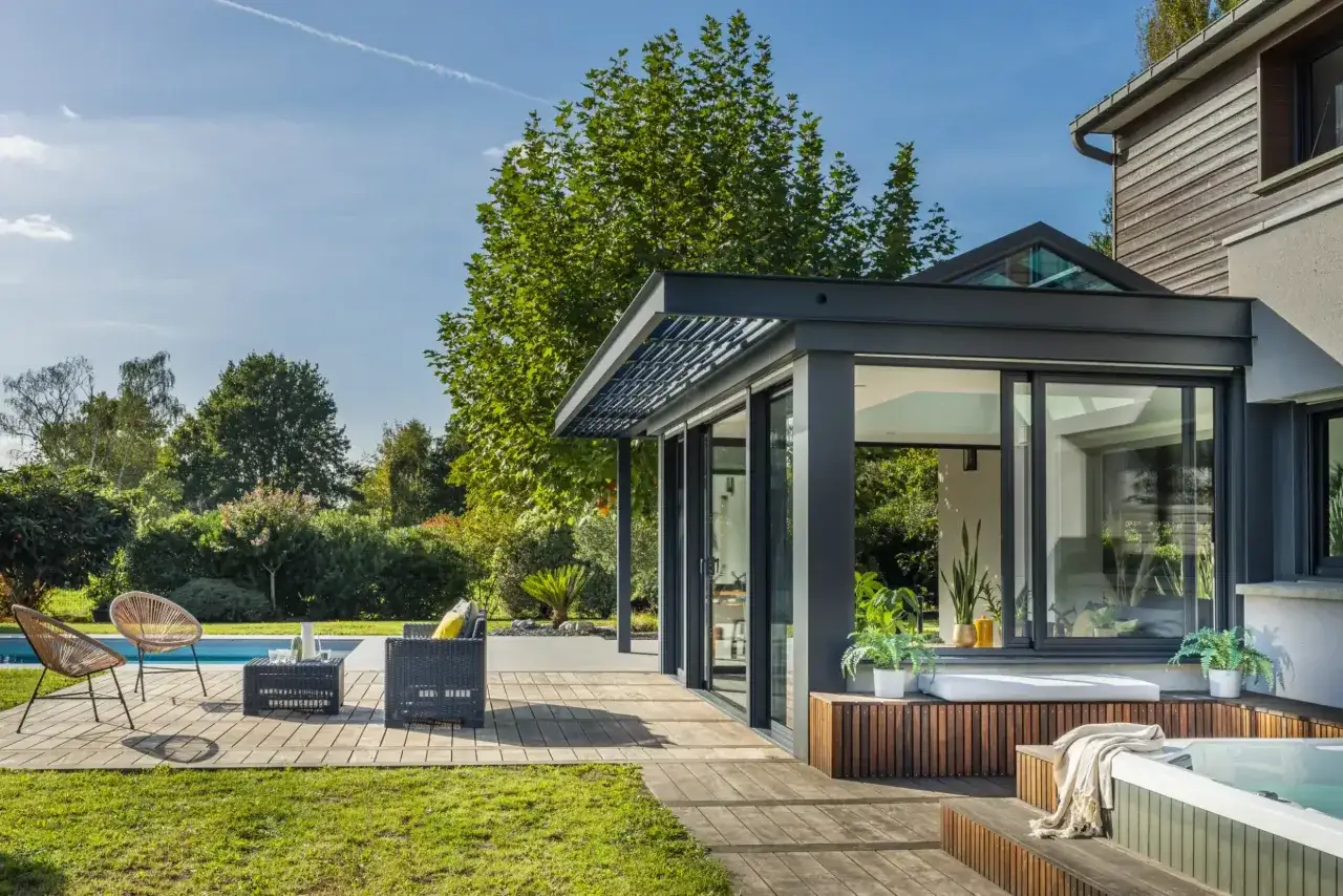 Une annexe maison moderne avec une verri&egrave;re, un jacuzzi et une piscine, entour&eacute;e d'un jardin luxuriant.