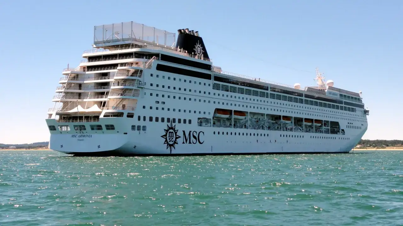 MSC Armonia, una nave da crociera imponente, solca le acque turchesi. La sua lunghezza è impressionante, con ponti multipli e oblò che si estendono lungo lo scafo bianco.