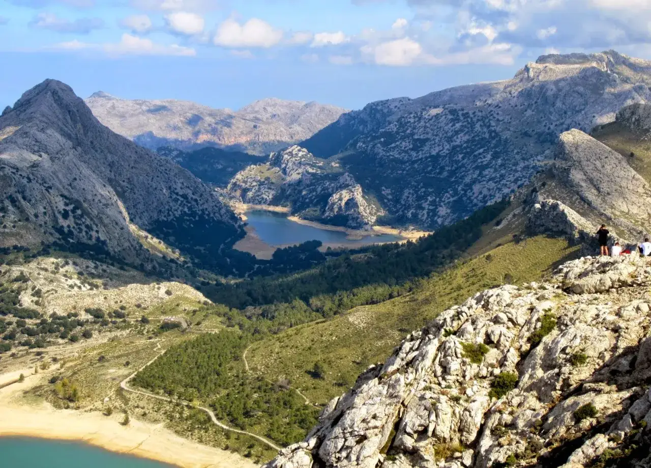 Disfruta del senderismo en Palma de Mallorca, con vistas a un valle verde y un lago azul rodeado de montañas rocosas.