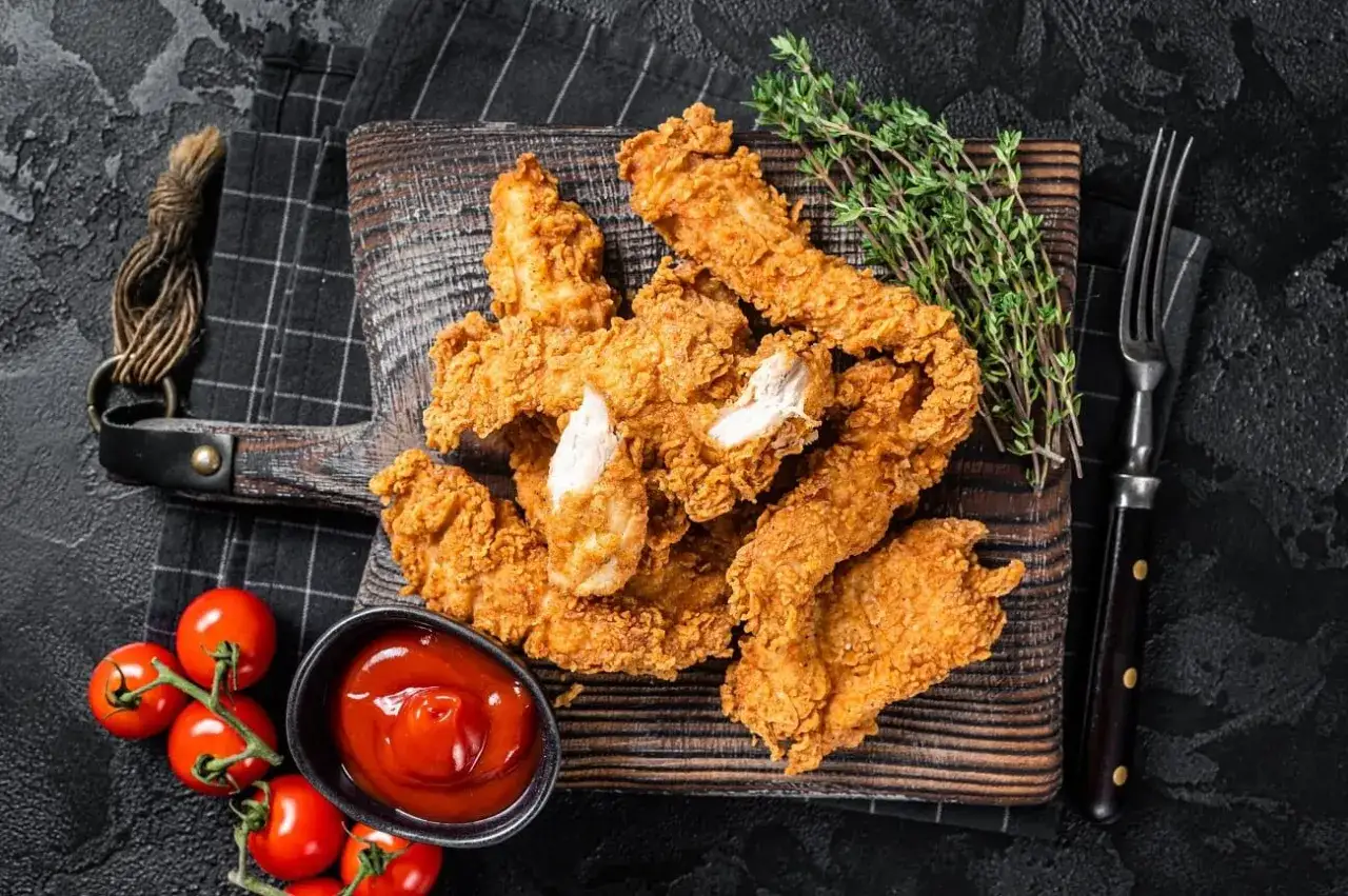 Knusprige Chicken-Streifen auf Holzbrett, serviert mit Ketchup und Kirschtomaten. Ein Genuss f&uuml;r jeden Liebhaber von crispy chicken.