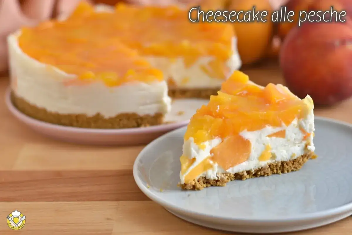 Una fetta di cheesecake alle pesche, con la torta intera sullo sfondo. La base croccante &egrave; sormontata da una crema soffice e pezzi di pesca succosa.
