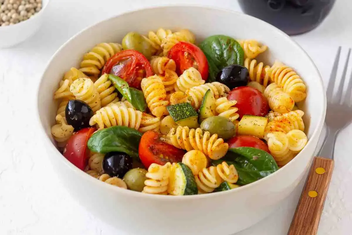 Una ciotola di pasta fredda saporita con fusilli, pomodorini, olive, zucchine e basilico fresco.