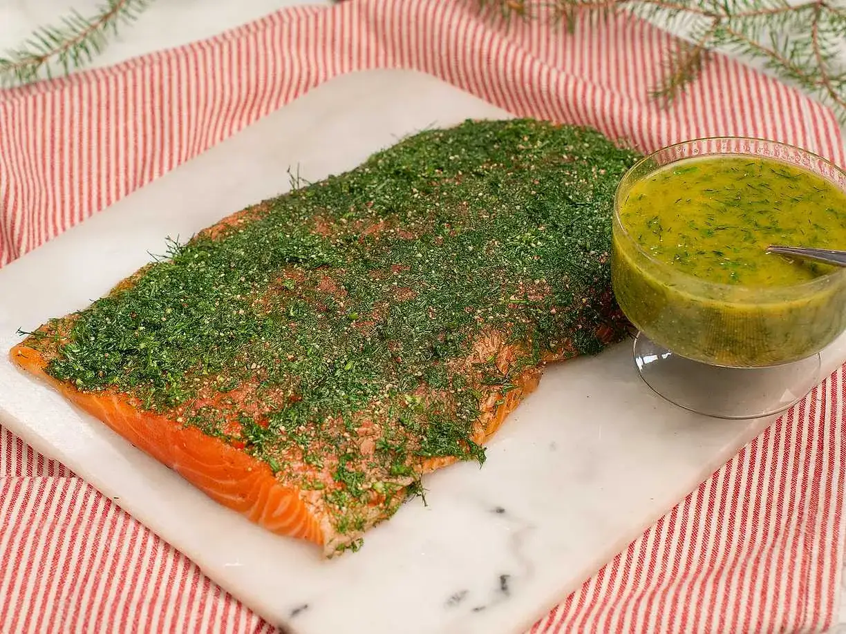 En bit gravad lax, täckt med dill och kryddor, bredvid en skål med gravlaxsås. Enkel guide till hur gravar man lax.