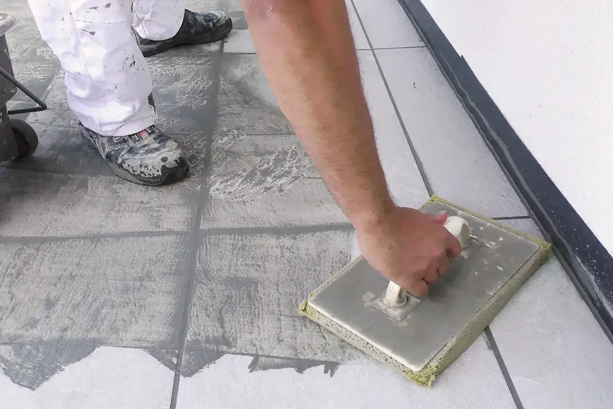 Arbeiter verfugt Terrassenplatten mit einem Schwammbrett. Die Fugenmasse wird gleichm&auml;&szlig;ig verteilt, um ein sauberes Ergebnis zu erzielen.